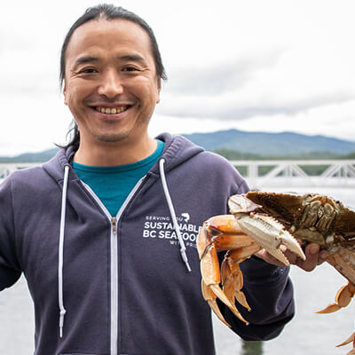 Chef Dai Fukasaku in a blue hoodie, smiling and holding a crab.