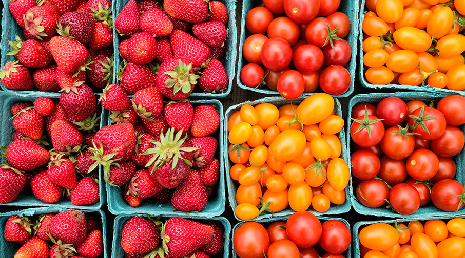 Aerial view of cartons of strawberries and red and orange cherry tomatoes.