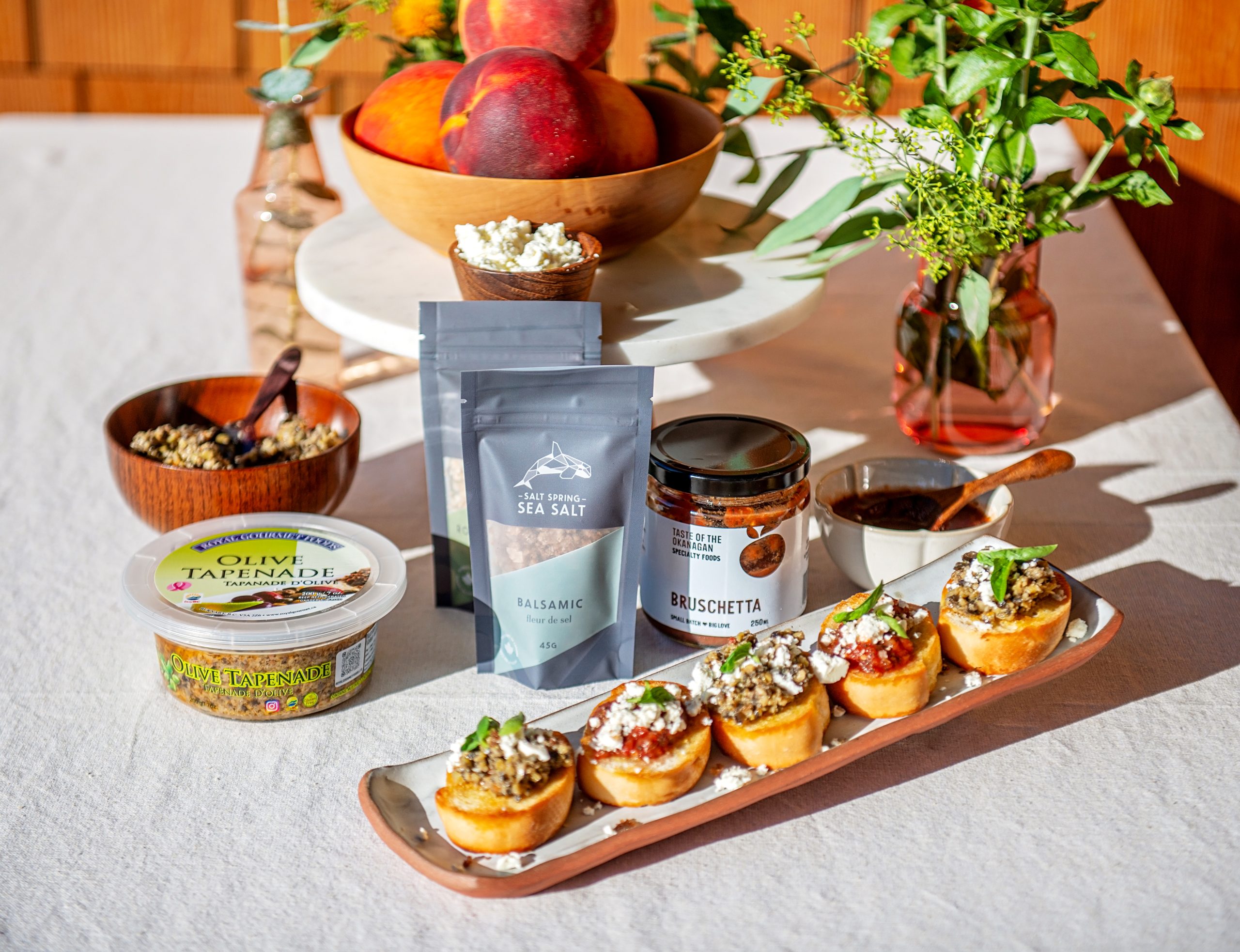 A beautiful summer appetizer display of bruschetta featuring Buy BC products: Royal Gourmet Foods Olive Tapenade, Taste of the Okanagan's Bruschetta Mix, and Salt Spring Sea Salt's Balsamic Fleur de Sel. 