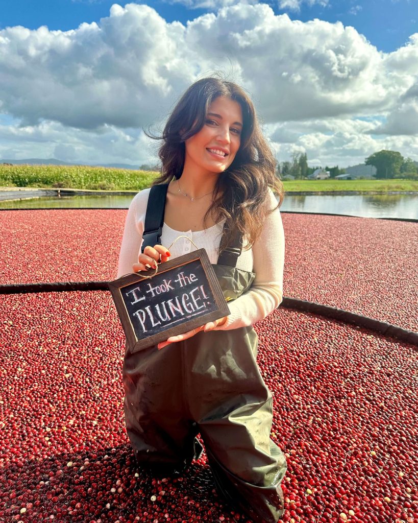 Chanelle Sullivan Saks standing in a flooded cranberry bog holding a sign that reads I took the plunge. 