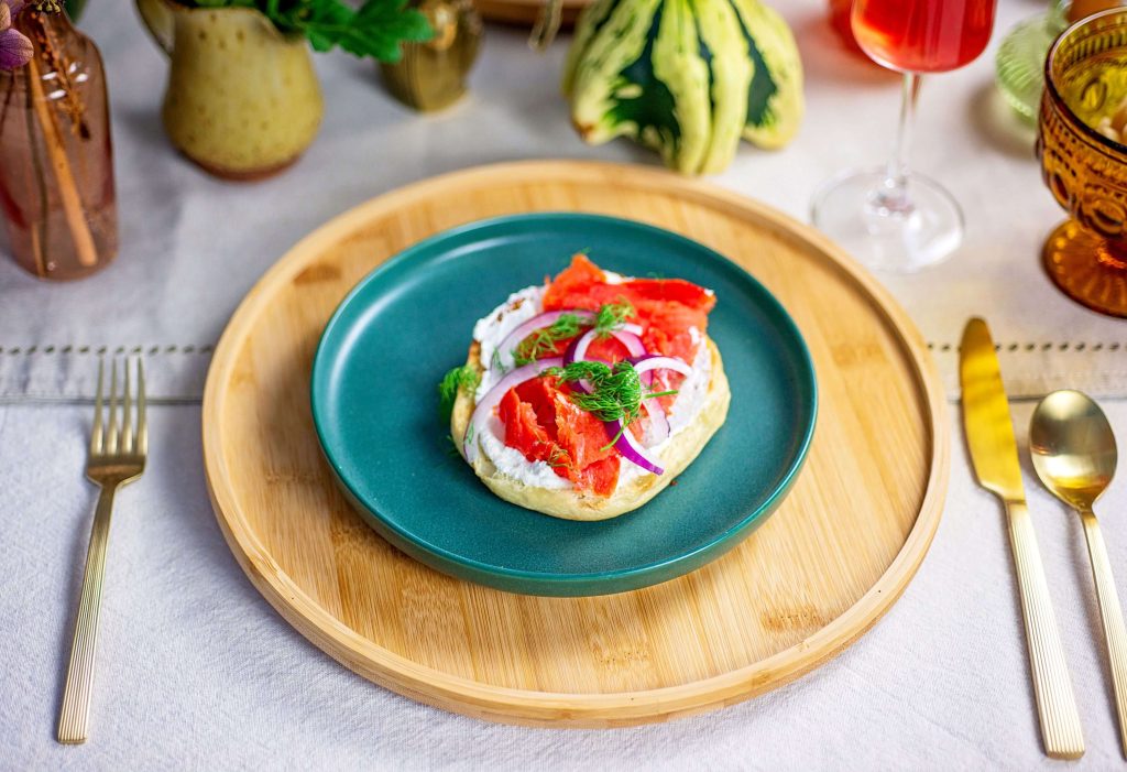 Fall brunch table setting featuring a bagel topped with cream cheese, wild B.C. salmon, red onion and fresh dill.