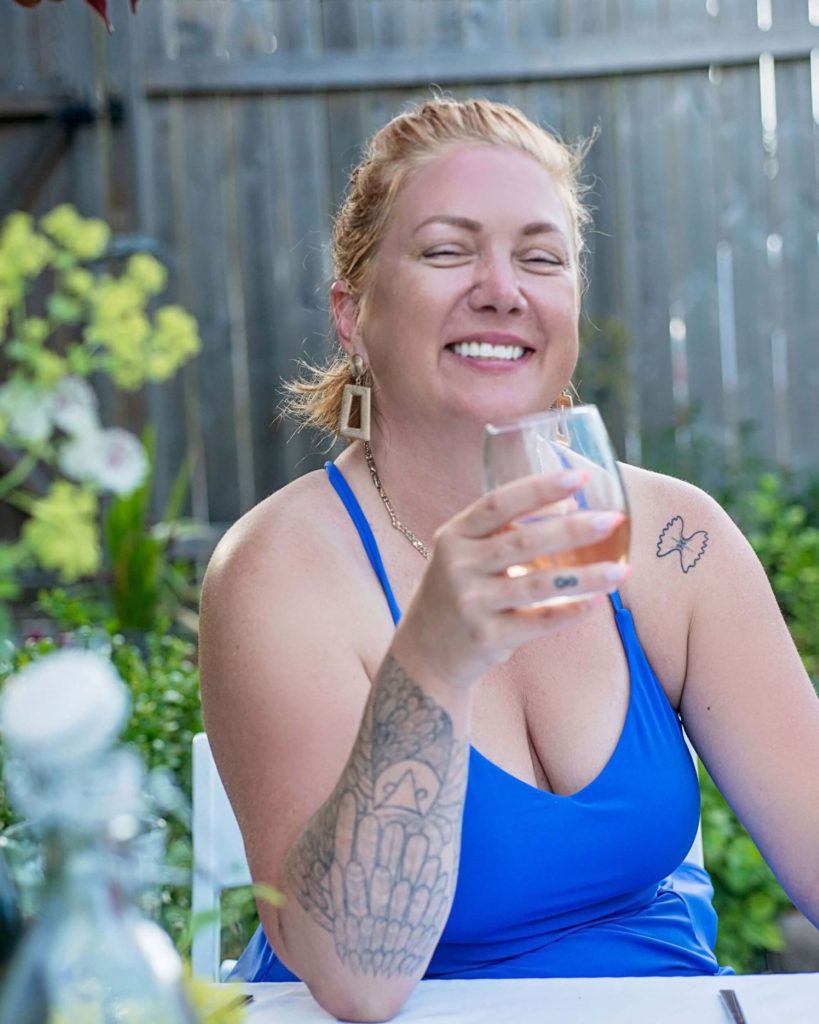 Danika McDowell sitting at a dinner table and holding a glass in a backyard garden setting during summer.