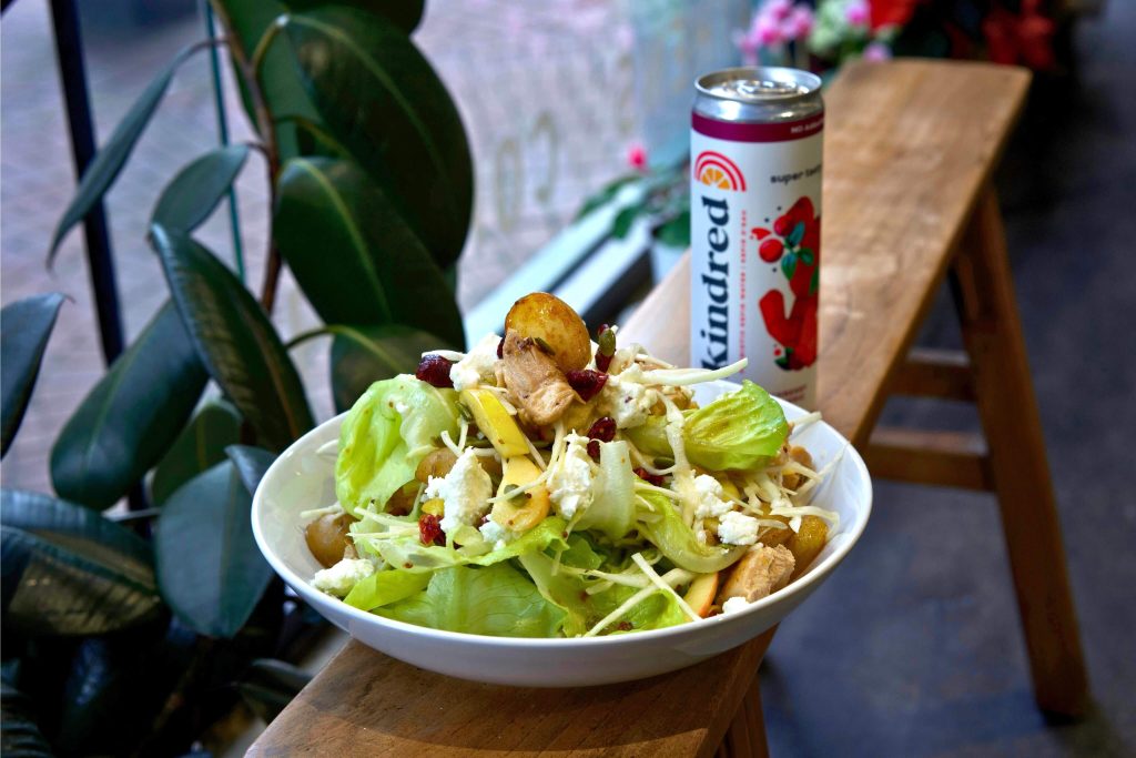 A bowl of a hearty winter B.C. salad on a bench beside a can of  Kindred Cultures Cranberry Turmeric Kefir Water.