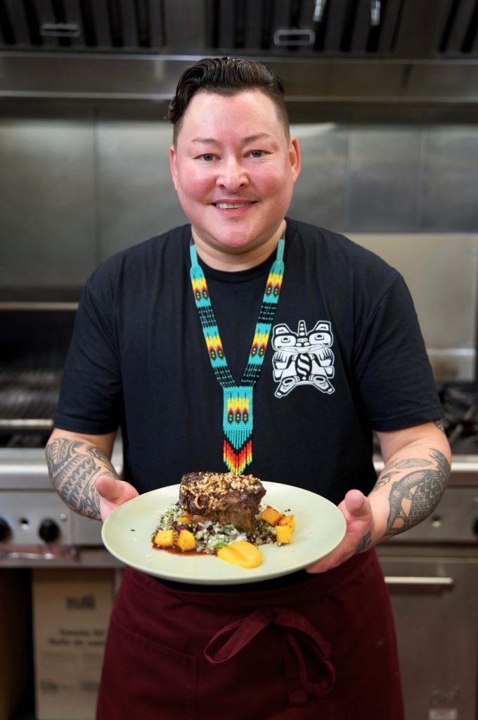 Indigenous chef holds plate of prepared B.C. bison in a professional kitchen