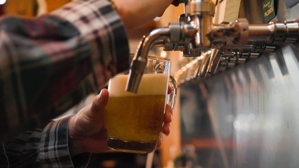 A close up of hands pouring draft B.C. beer into a glass mug.