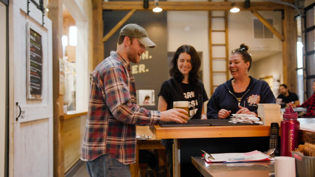 Three people gather around a bar and look down at large mugs of B.C. beer.
